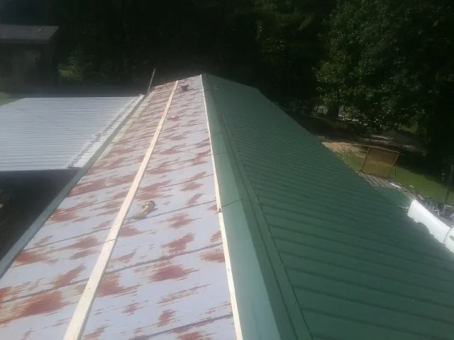 Old rusted panels beside newly installed green metal roofing — Wind Damage Roof Repair by Roofing Brothers in Millville